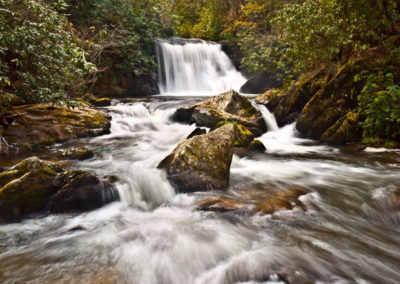 A serene waterfall cascades over rocky outcrops into a winding river