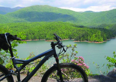 A mountain bike rests on a cliffside overlooking a serene lake