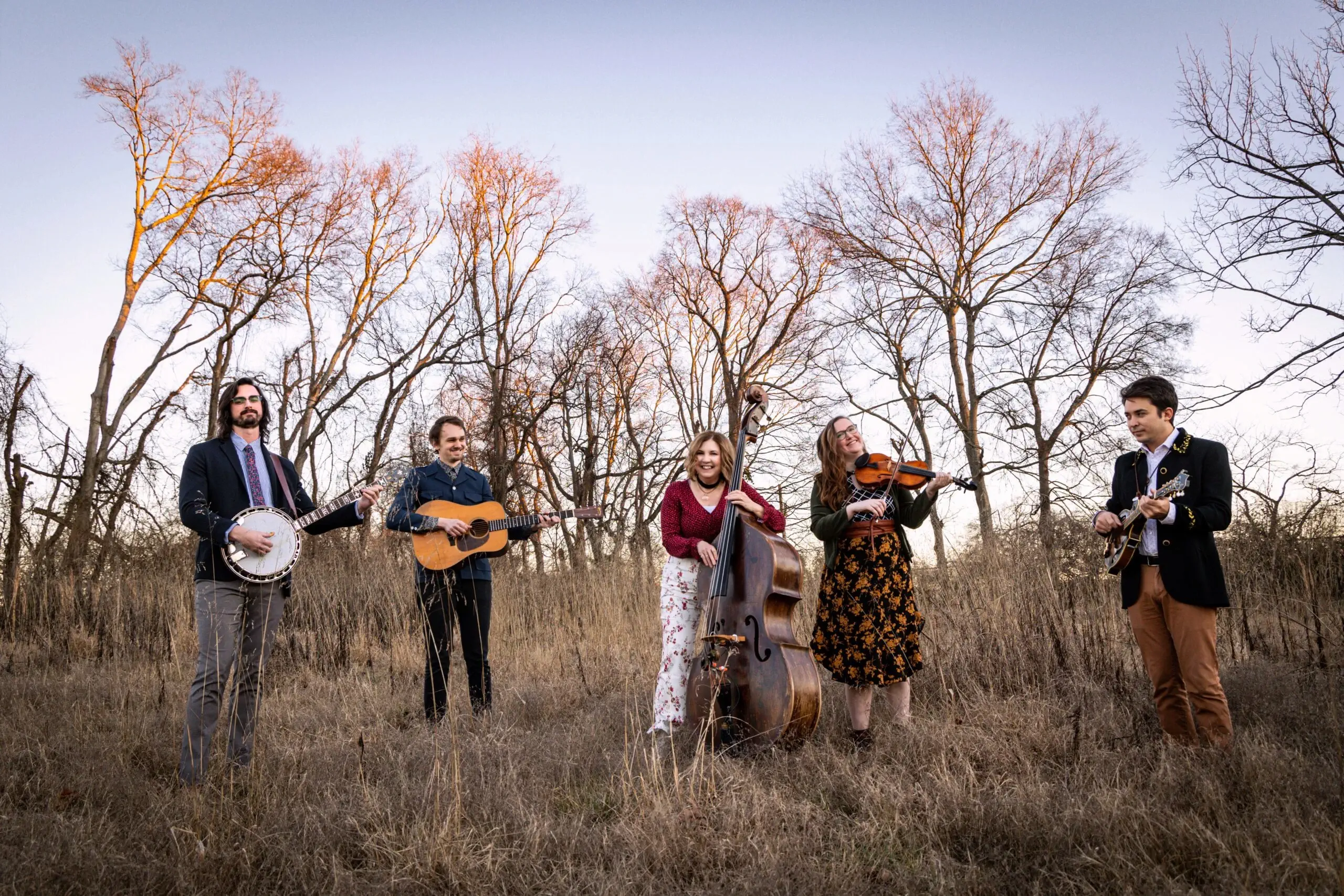 A group of five musicians play outdoors in tall grass