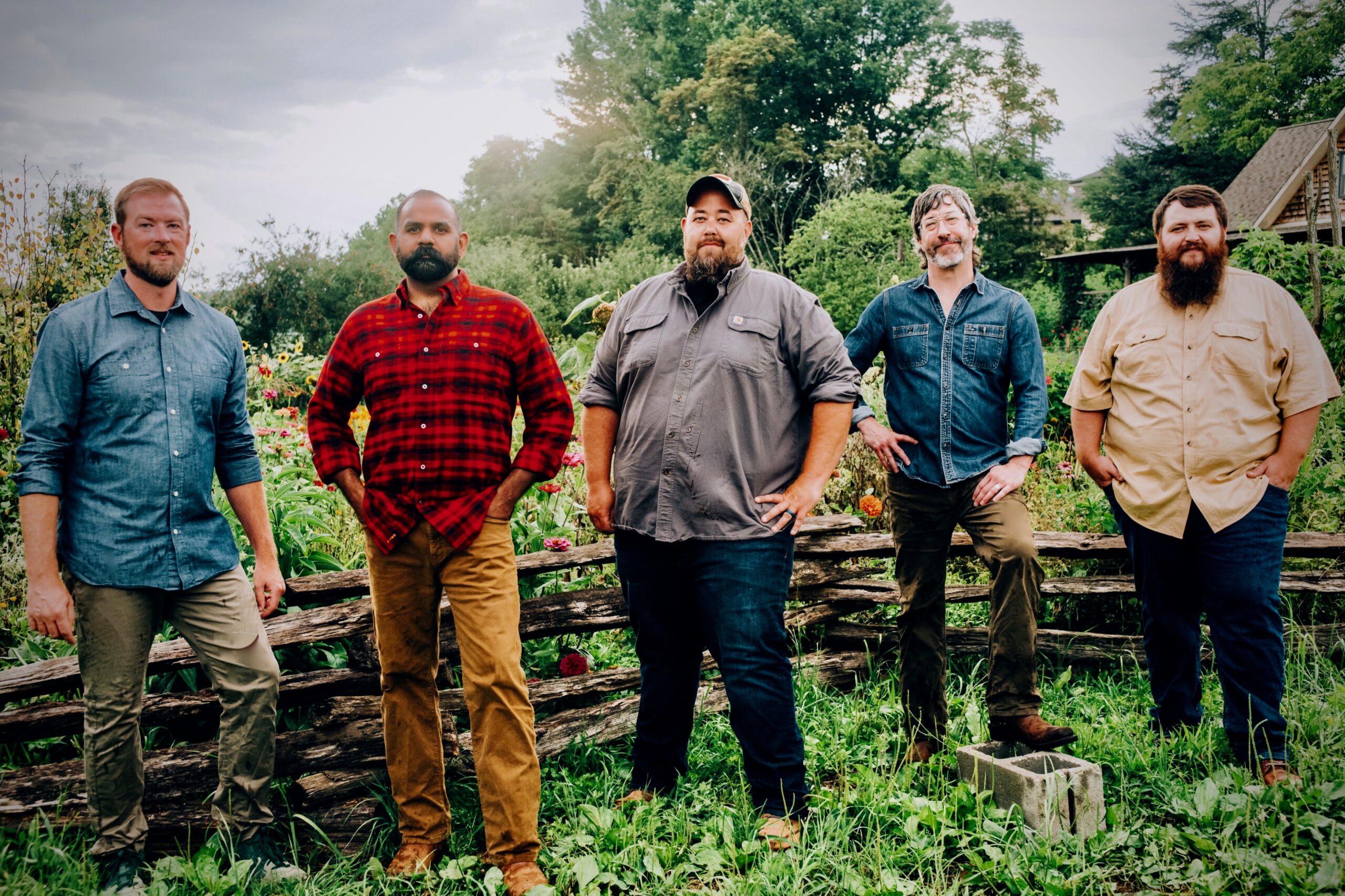 Five men stand confidently in a lush garden