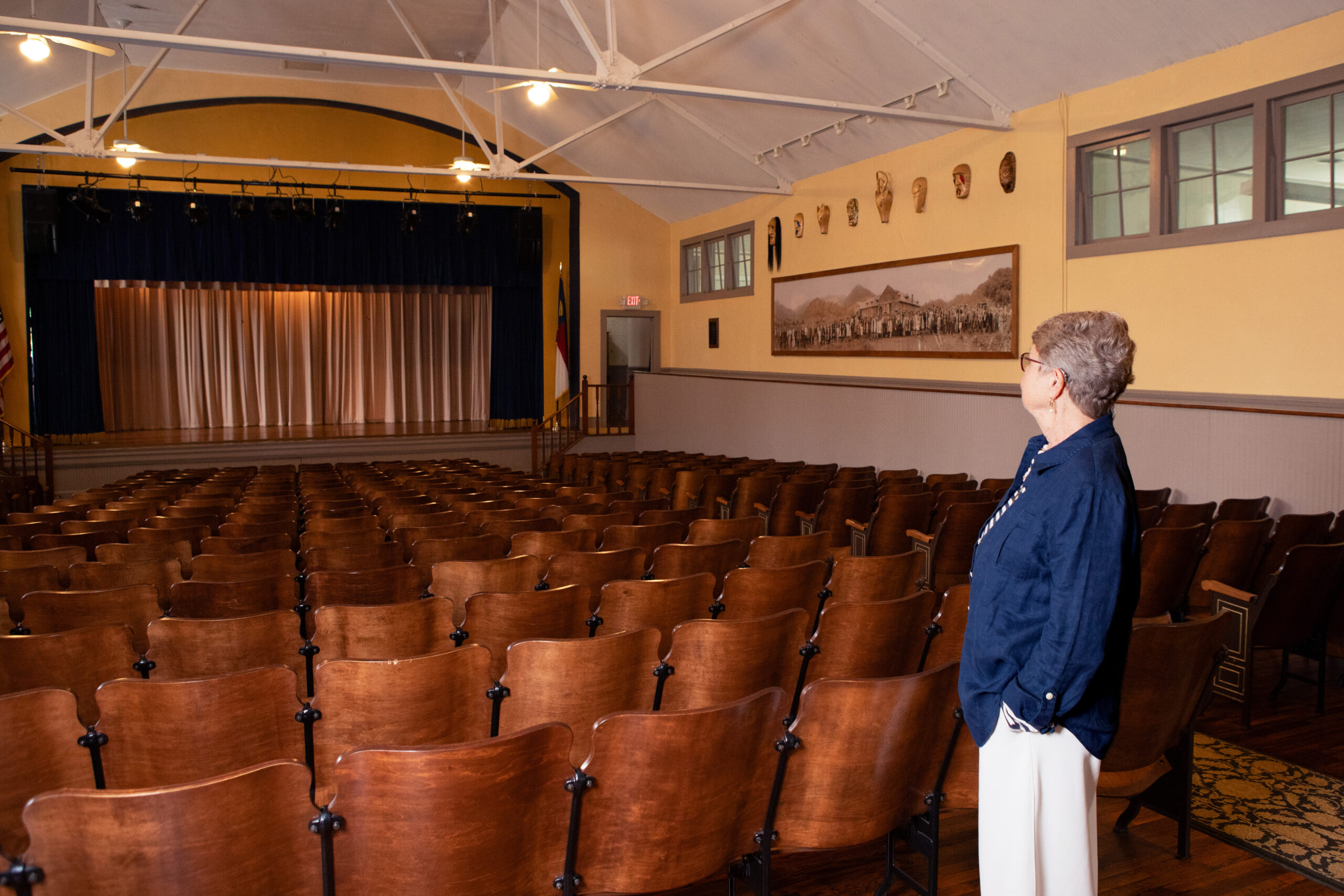 First Director of Stecoah, Lynn Shields looking toward the stage of the auditorium with rows of wooden seats in front of her