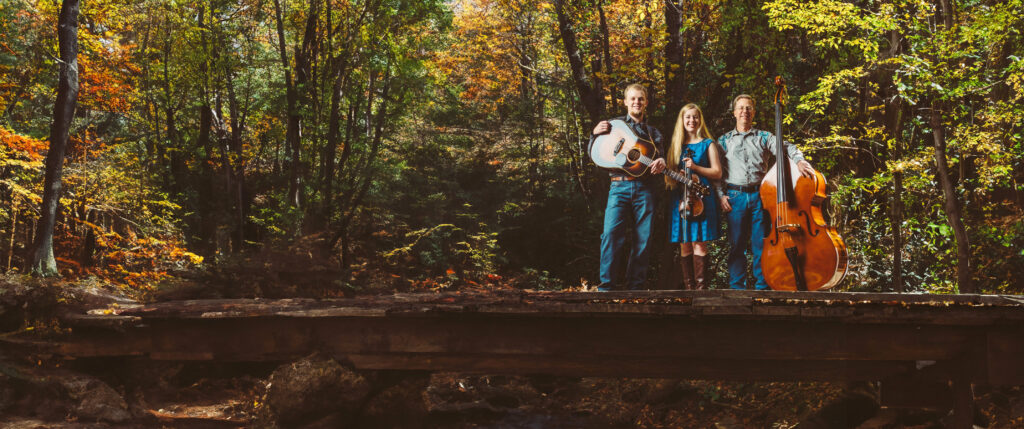 Snyder family band standing on a bridge in front of fall leaves.