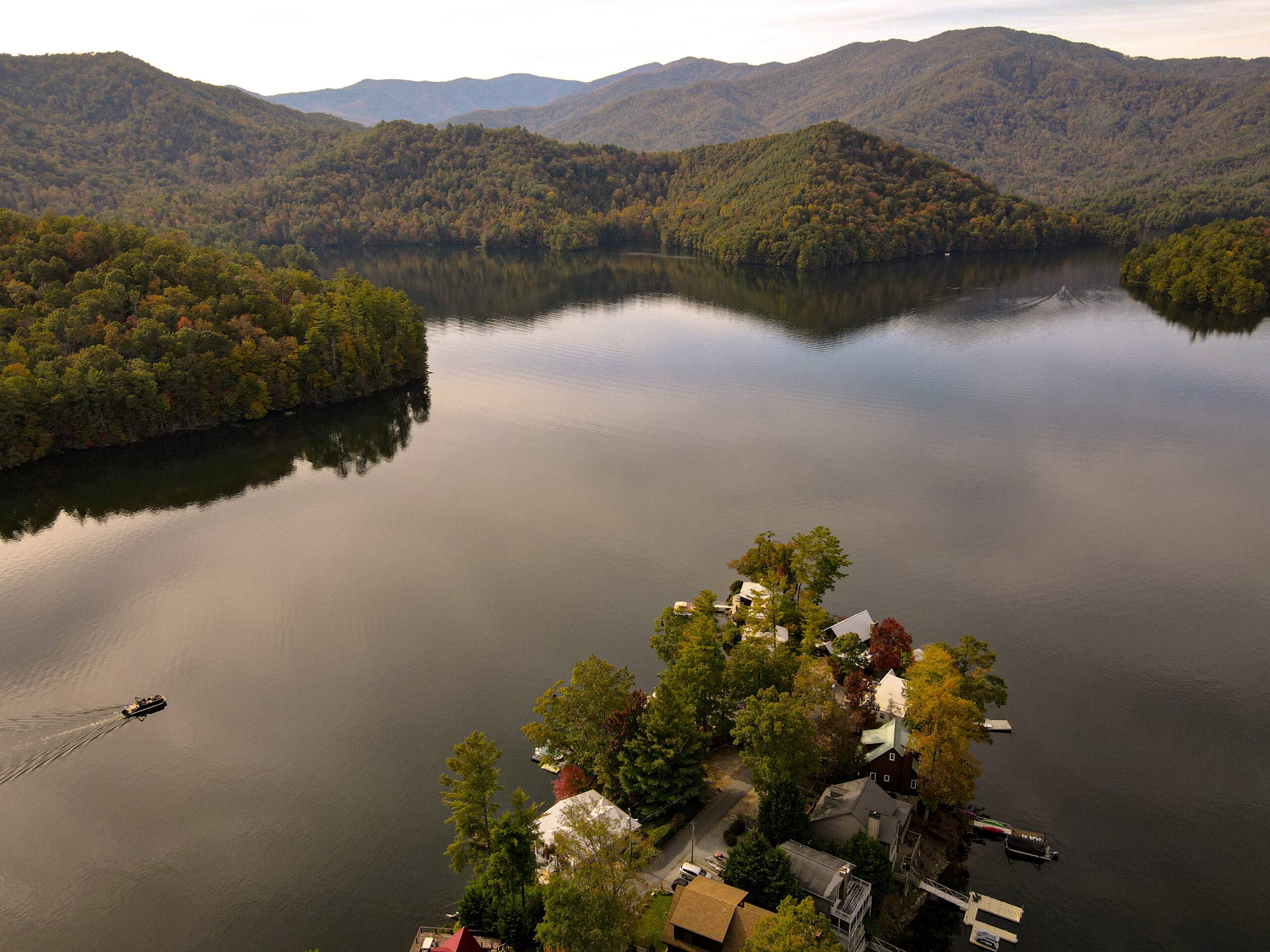 Lake Santeetlah in Fall with Boat in motion and a few houses on the shore.