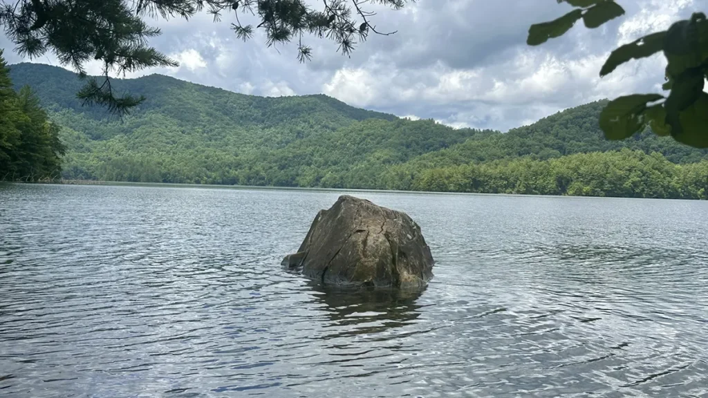 Calm summer water on Lake Santeetlah seen from the shoreline at Cheoah Point, a put-in spot for paddlers, with green ridges across the lake.